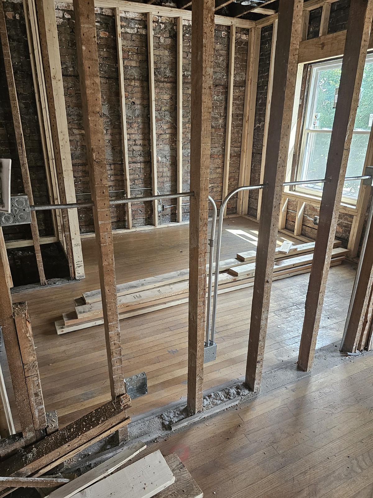 Interior gut rehab showing new stud framing, exposed brick, and original hardwood floors